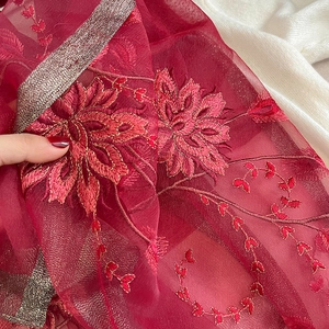 Détail d'un châle en soie et laine rouge avec broderies florales et bordures dorées