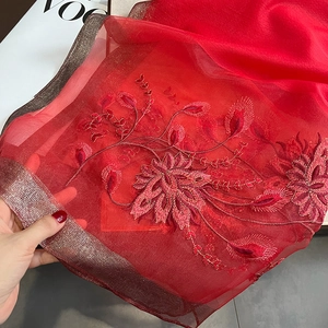 Détail d'une écharpe en soie et laine rouge avec broderie florale et texture légère