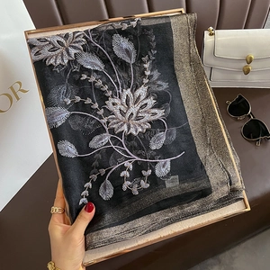 Détail d'une écharpe en soie noire avec broderies florales argentées et bords dorés