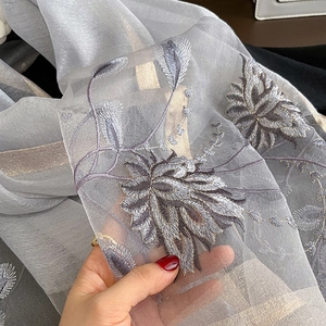 Détail macro d'un tissu transparent léger avec broderie florale et fines rayures métalliques