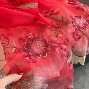 Detail of red floral embroidery on sheer fabric with shimmering metallic edge finish
