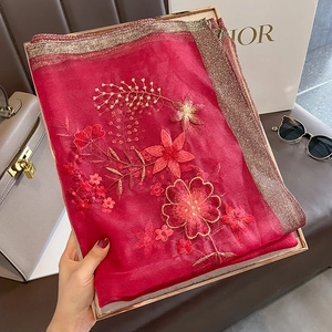 Detail of red silk wool scarf featuring floral embroidery and golden thread edging