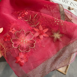 Detail of red silk wool shawl featuring intricate gold floral embroidery and metallic edges
