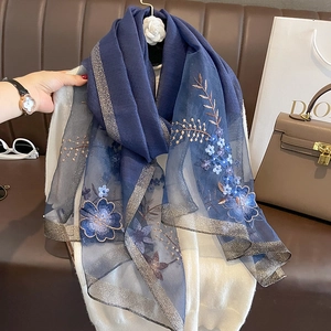 Detailed close-up of blue floral embroidery on navy silk wool scarf with gold trim