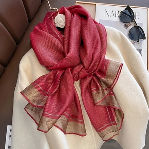 Elegant red silk scarf with gold stripes draped on a white coat for a stylish winter look