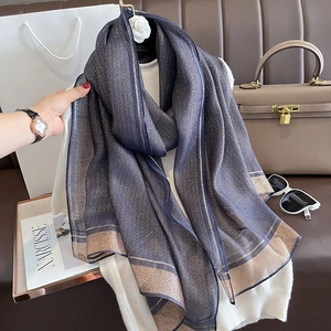 Detail of navy blue silk scarf with metallic gold stripes draped on white sweater