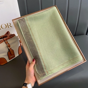 Detail of light green silk scarf with metallic gold woven edges in a wooden tray