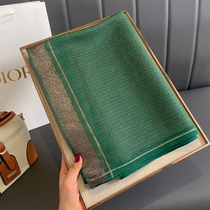 Green silk scarf with gold stripes folded in a gold gift box on a luxury background