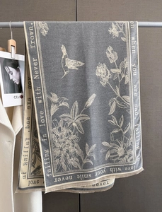 Detailed view of grey scarf featuring floral prints and hummingbird pattern with fringed edges