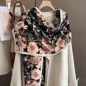 Écharpe en cachemire à fleurs noir et orange sur un manteau blanc suspendu sur un cintre