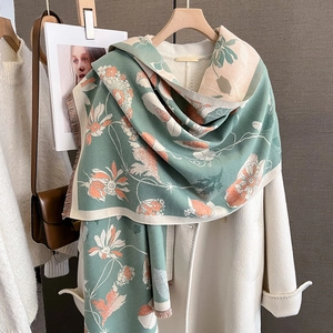 Détail d'une écharpe en jacquard floral vert sauge avec franges sur un manteau blanc