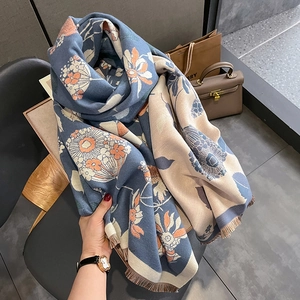 Détail d'une écharpe fleurie bleue et beige montrant le tissage jacquard et les franges