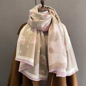 Détail d'une écharpe fleurie style cachemire avec franges portée sur un manteau marron