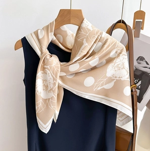 Écharpe en soie champagne à pois et fleurs stylisée sur une robe bleu foncé sur cintre