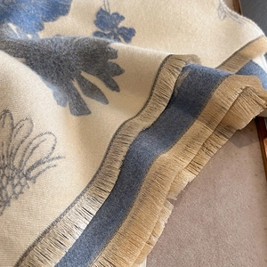 Detailed view of luxury cashmere-like scarf with blue floral patterns and fine fringe trim