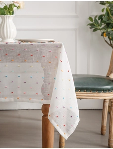 Detail of colorful tufted pom-poms on a white textured jacquard tablecloth for dining decor