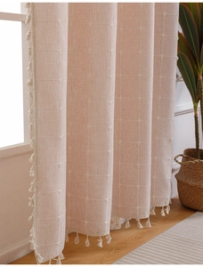 Detail of coral pink linen curtain with white cross-stitch grid and delicate fringe tassels