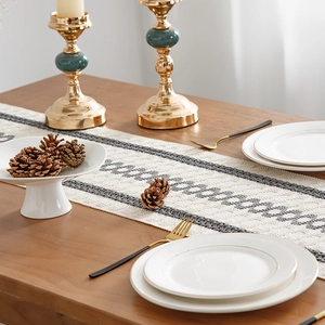 Linen striped table runner with tassels on wood table with candles and pine cones