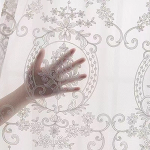 Detailed close-up of white floral embroidery on translucent lace sheer curtain fabric