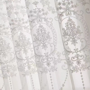Close-up of white sheer curtain fabric featuring intricate floral embroidery and textures