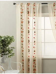 Detailed close-up of beige semi-sheer lace curtain with festive red bell embroidery