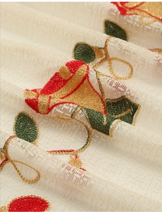 Detail of beige sheer curtain with festive red and gold bell embroidery on mesh fabric