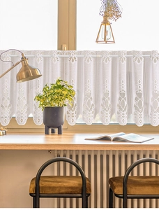 Detail of white lace cafe curtain featuring intricate floral patterns and scalloped edges