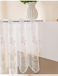 Detail of white lace cafe curtain with colorful butterfly embroidery and scalloped edge