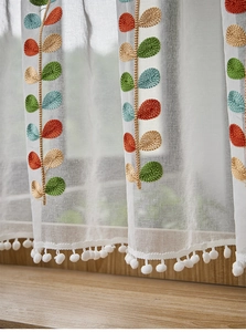 Detailed close-up of white sheer curtain with colorful leaf embroidery and pom-pom trim