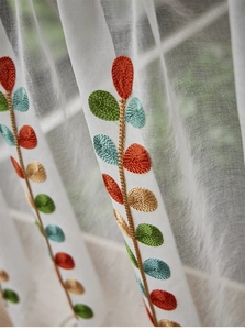 Macro view of colorful floral embroidery on white sheer semi-transparent fabric curtain