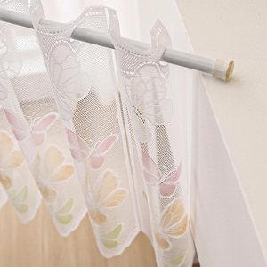 White lace cafe curtain with colorful butterfly patterns hanging on a tension rod