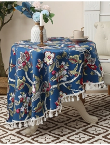 Detailansicht einer runden Vintage-Tischdecke mit Blumenmuster und weißen Quasten