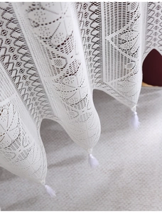 Close-up of white lace curtain valance with intricate floral patterns and cotton tassels