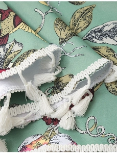 Detail der hellgrünen Tischdecke mit Blumenmuster und weißen Quasten am Rand