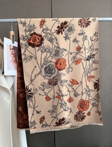 Detailed view of beige cashmere-feel scarf with artistic orange floral prints and fringe