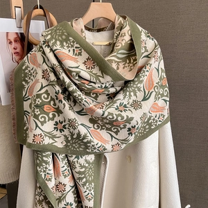 Detail of floral knit scarf with tulip pattern and tassels draped on a white coat