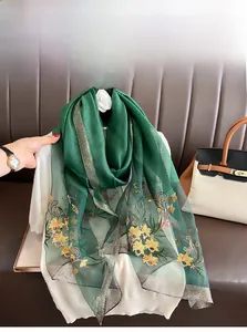 Close-up of dark green silk scarf featuring delicate yellow floral embroidery and gold edges