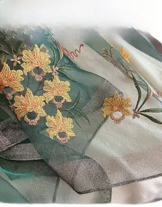 Detail of dark green silk scarf featuring yellow floral embroidery and machine-stitched edges