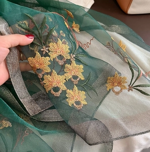 Detailed embroidery of yellow flowers on a sheer dark green silk wool scarf