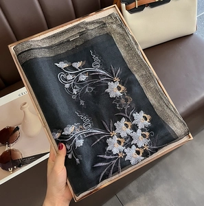 Detailed close-up of floral embroidery on a black silk wool scarf in a gift box