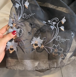 Detail of floral embroidery on sheer black silk-wool scarf with gold metallic trim
