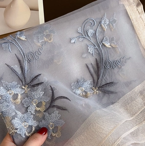 Detailed close-up of light grey silk wool scarf featuring intricate floral embroidery