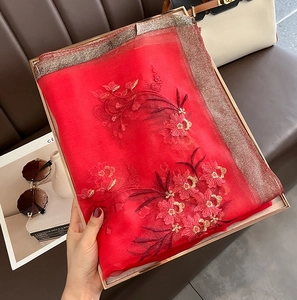 Detail of red silk wool scarf featuring golden floral embroidery and metallic edges