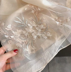 Detail of silk wool scarf showing delicate 3D floral embroidery on champagne gauze