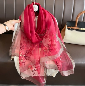 Detail of red silk wool scarf featuring floral embroidery and golden shimmering edges