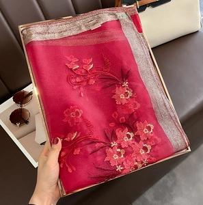 Macro detail of red silk wool scarf with floral embroidery in a luxury gift box
