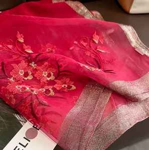 Macro shot of red silk scarf featuring exquisite floral embroidery and golden thread edges