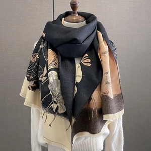 Thick winter scarf with ginkgo leaf print and fringes draped on a white sweater
