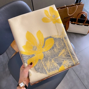 Detailed view of folded mustard green silk scarf with yellow lotus print in a gift box