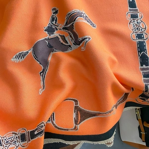 Detail view of equestrian pattern scarf with orange horse motifs and fringe edges